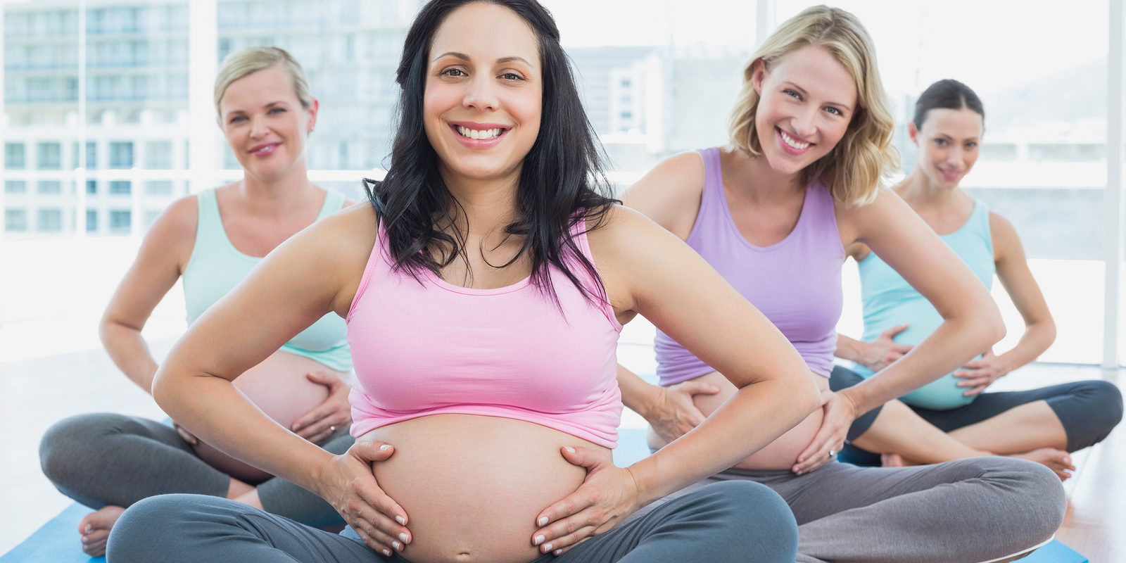 Happy pregnant women in yoga class holding their bumps in a fitn