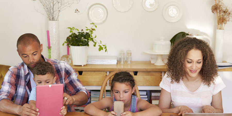 Family Sitting Around Table At Home Using Technology